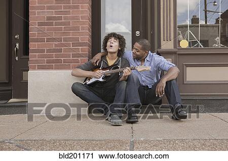 Stock Image - Father watching son playing electric guitar. Fotosearch