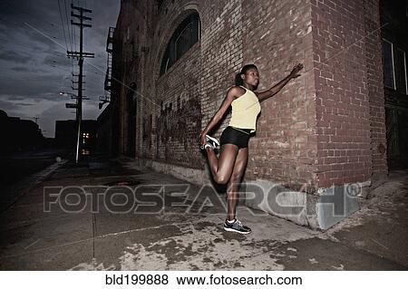 Stock Photo - Female athlete stretching on sidewalk. Fotosearch