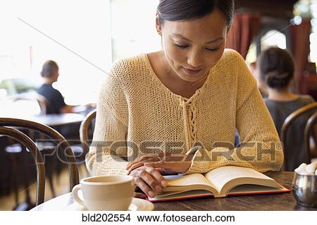 Picture - Filipino woman reading book in cafe. Fotosearch