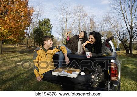 Stock Photo - Friends eating pizza in back of truck. Fotosearch