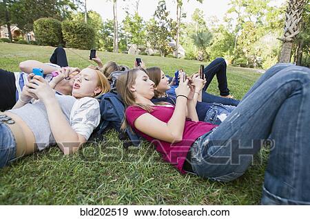 Stock Photo - Friends hanging out together on grass using cell phones. Fotosearch