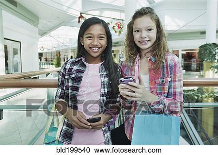 Stock Image - Friends holding cell phones in shopping mall. Fotosearch