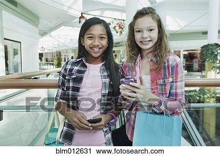 Stock Image - Friends holding cell phones in shopping mall. Fotosearch