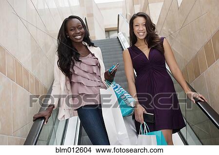 Friends holding shopping bags on escalator View Large Photo Image Picture - Friends holding shopping bags on escalator. Fotosearch