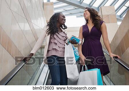 Stock Image - Friends holding shopping bags on escalator. Fotosearch