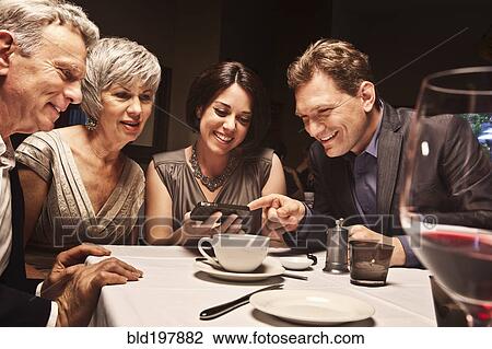 Friends looking at camera phone in restaurant View Large Photo Image Stock Image - Friends looking at camera phone in restaurant. Fotosearch