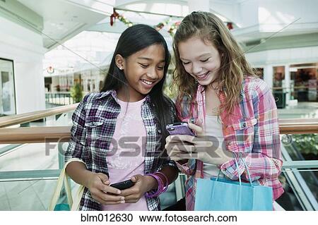 Friends looking at cell phone in shopping mall View Large Photo Image Stock Image - Friends looking at cell phone in shopping mall. Fotosearch