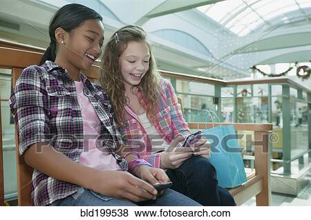 Friends looking at cell phone in shopping mall View Large Photo Image Stock Photo - Friends looking at cell phone in shopping mall. Fotosearch