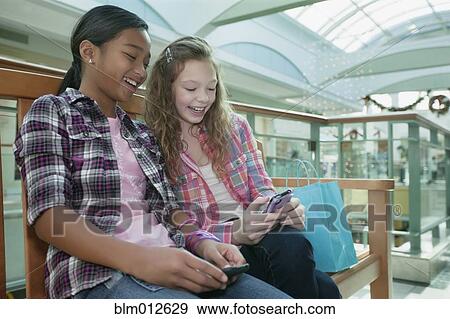 Friends looking at cell phone in shopping mall View Large Photo Image Stock Photo - Friends looking at cell phone in shopping mall. Fotosearch