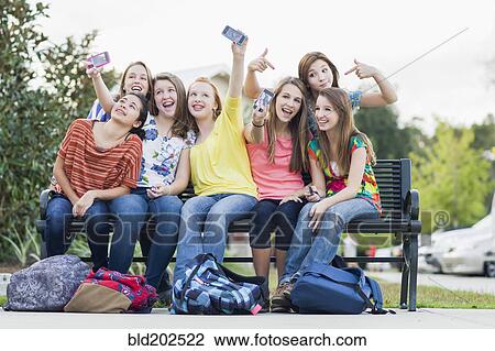 Stock Image - Friends on bench taking self-portraits with cell phones. Fotosearch