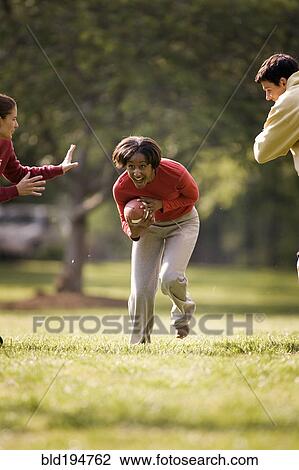 Stock Image - Friends playing football in park. Fotosearch