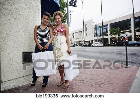 Friends standing on city sidewalk holding shopping bags View Large Photo Image Stock Photography - Friends standing on city sidewalk holding shopping bags. Fotosearch