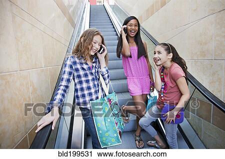Stock Image - Friends using cell phones on shopping mall escalator. Fotosearch