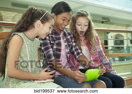 Friends using digital tablet in shopping mall View Large Photo Image Stock Photo - Friends using digital tablet in shopping mall. Fotosearch
