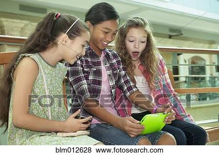 Stock Photo - Friends using digital tablet in shopping mall. Fotosearch