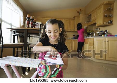 Stock Photography - Girl using toy iron and ironing board in kitchen. Fotosearch