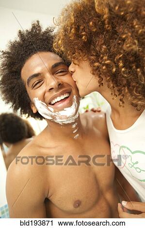 Stock Image - Girlfriend kissing boyfriend's shaving cream-covered face. Fotosearch