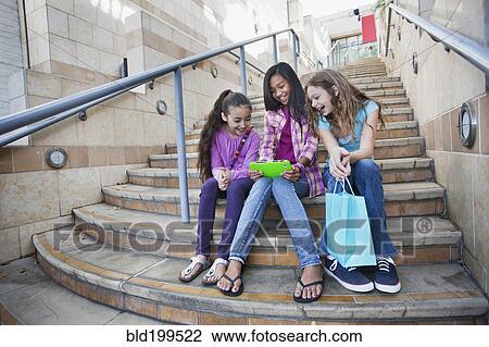Girls sitting on steps sharing digital tablet View Large Photo Image Stock Image - Girls sitting on steps sharing digital tablet. Fotosearch
