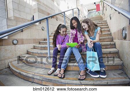 Stock Image - Girls sitting on steps sharing digital tablet. Fotosearch