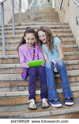Girls using digital tablet on staircase View Large Photo Image Stock Photo - Girls using digital tablet on staircase. Fotosearch