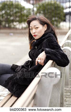 Stock Image - Glamorous Korean woman sitting on bench. Fotosearch