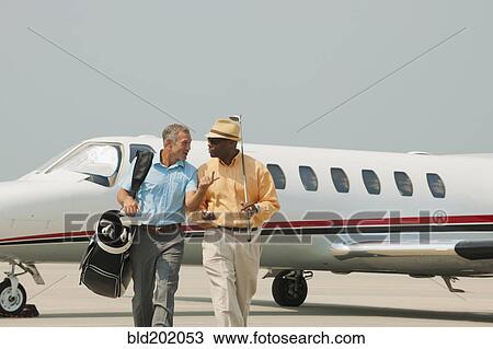 Stock Image - Golfers walking on airport tarmac. Fotosearch