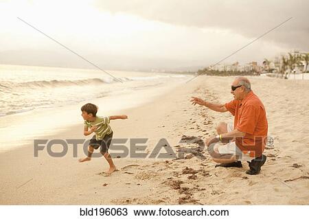 Stock Image - Grandfather and grandson playing on beach together. Fotosearch