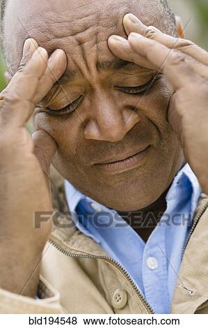 Stock Photo - Grimacing mixed race man rubbing forehead. Fotosearch