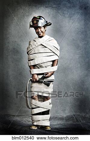 Stock Image - Grinning firefighter tied up in fire hose. Fotosearch