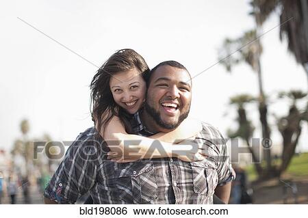 Stock Photograph - Grinning man giving wife piggyback ride. Fotosearch