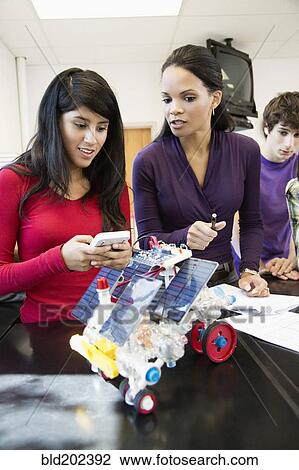 Stock Image - High school students working on solar powered machine in classroom. Fotosearch
