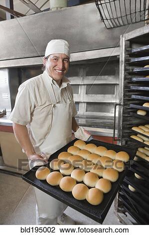 Stock Image - Hispanic baker holding tray with bread. Fotosearch