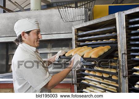 Stock Image - Hispanic baker holding tray with bread. Fotosearch