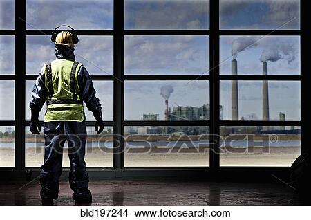 Picture - Hispanic construction worker looking out window at factory. Fotosearch