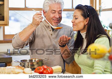 Stock Image - Hispanic couple cooking together in kitchen. Fotosearch