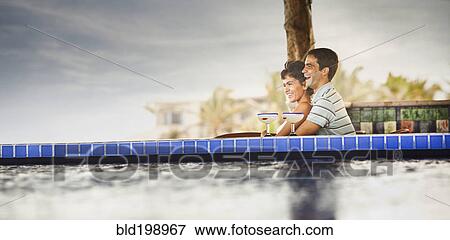 Stock Photo - Hispanic couple drinking cocktails at poolside. Fotosearch