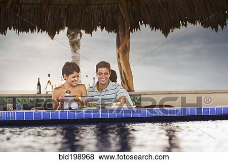 Stock Photo - Hispanic couple having dinner at poolside. Fotosearch