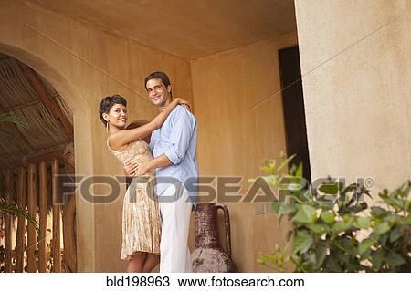 Stock Image - Hispanic couple hugging on front stoop. Fotosearch
