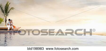 Stock Image - Hispanic couple relaxing near swimming pool. Fotosearch
