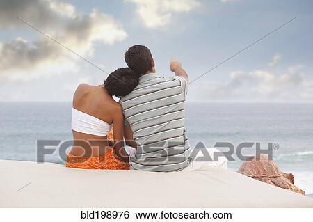 Stock Photograph - Hispanic couple sitting and looking at ocean. Fotosearch