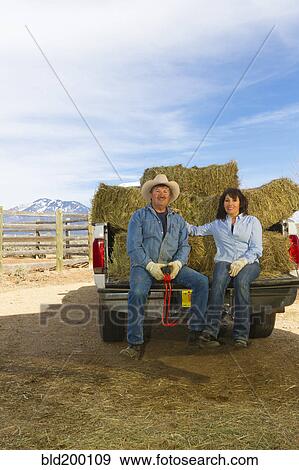 Stock Photo - Hispanic couple sitting on back of truck full of hay. Fotosearch