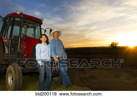 Hispanic couple standing near tractor on farm View Large Photo Image Stock Photo - Hispanic couple standing near tractor on farm. Fotosearch