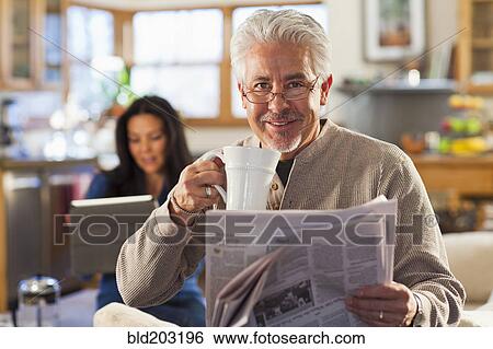 Stock Photograph - Hispanic man drinking coffee and reading newspaper. Fotosearch