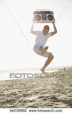 Stock Image - Hispanic man holding boom box and jumping. Fotosearch
