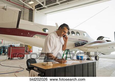 Stock Photograph - Hispanic man working in airplane hangar. Fotosearch