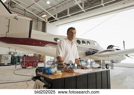 Stock Photography - Hispanic man working in airplane hangar. Fotosearch