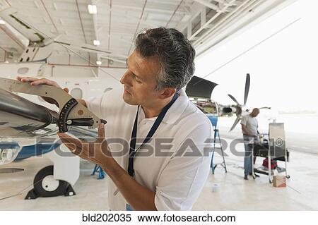 Stock Photography - Hispanic man working in airplane hangar. Fotosearch
