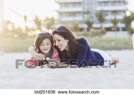 Stock Photograph - Hispanic mother and daughter laying on beach. Fotosearch