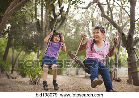 Stock Photo - Hispanic sisters swinging on swings. Fotosearch