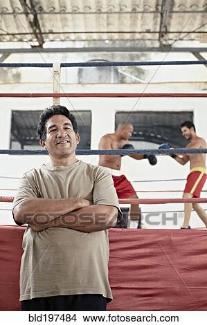 Picture - Hispanic trainer standing next to boxers fighting in ring. Fotosearch
